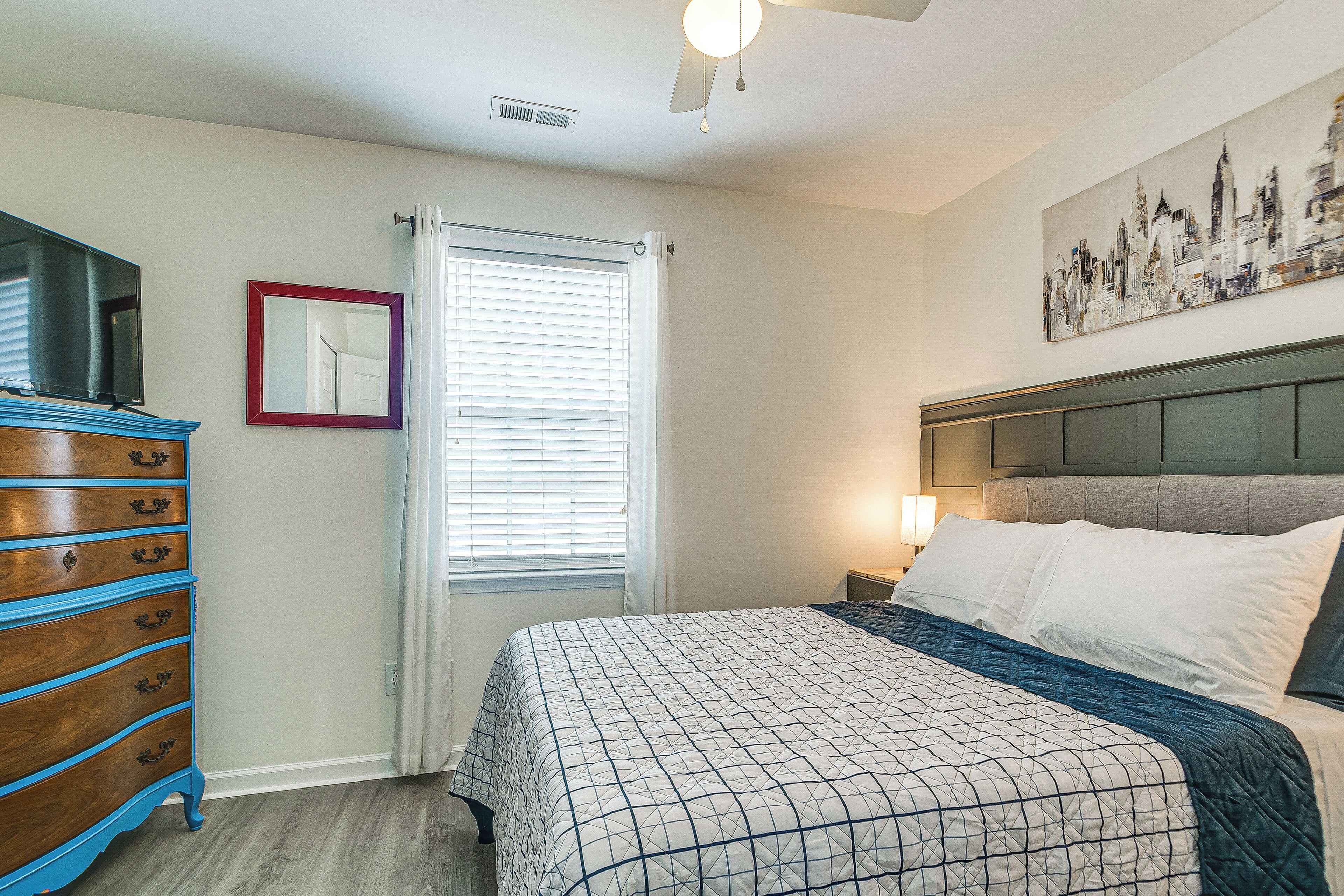 A bedroom with a bed, dresser, and artwork on the wall.