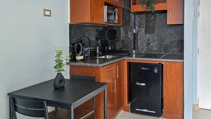 A compact kitchen with wooden cabinets, a black countertop, and a black refrigerator. - Modern studio close to Barrio Italia (Santiago)
