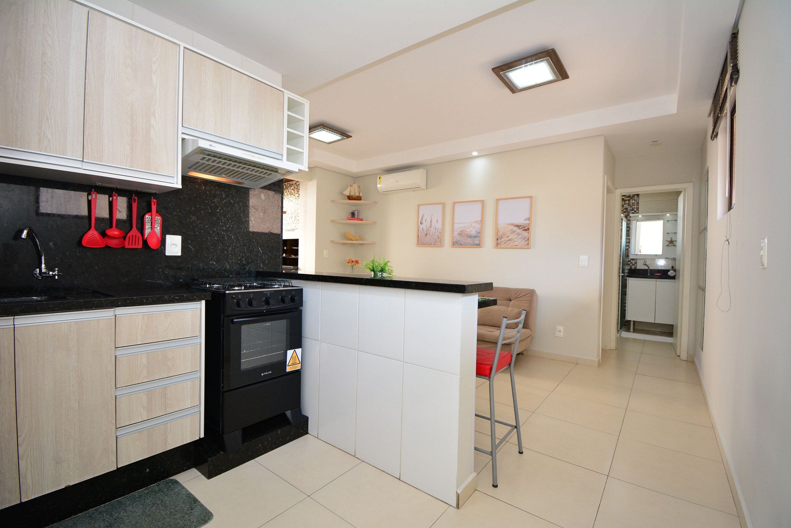 A modern kitchen with wooden cabinets, a black stove, and a white island. There is a red spatula hanging on the wall and a small plant on the island.