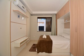 A bedroom with a bed, a wooden wardrobe, a built-in bench, and a window with a view of the outside. - Taiamã - Rua das Gaivotas - Ingleses (Florianópolis)