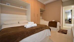 A bedroom with two beds, a wooden wardrobe, and a bathroom with a bathtub. - Taiamã - Rua das Gaivotas - Ingleses (Florianópolis)