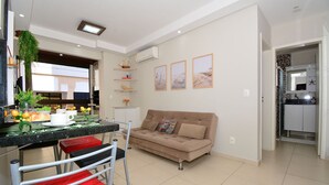 Un salon moderne avec un canapé, une table à manger et des chaises, et un coin cuisine visible à travers une porte ouverte.