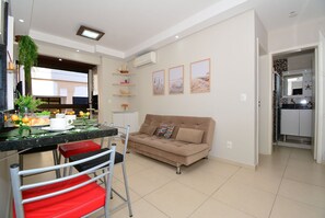 A modern living room with a sofa, a dining table with chairs, and a kitchen area visible through an open doorway. - Taiamã - Rua das Gaivotas - Ingleses (Florianópolis)