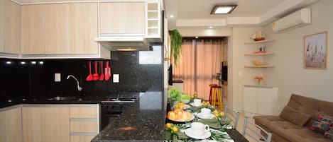 A modern kitchen with wooden cabinets, a black countertop, and a dining area with a table set for two.