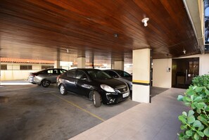 A covered parking area with cars, a building entrance, and a plant. - Taiamã - Rua das Gaivotas - Ingleses (Florianópolis)