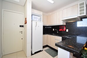 A kitchen with white cabinets, a black countertop, a microwave, a refrigerator, and a stove.