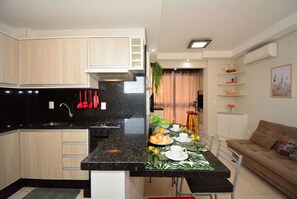 A modern kitchen with wooden cabinets, a black countertop, and a dining area with a table set for two. - Taiamã - Rua das Gaivotas - Ingleses (Florianópolis)