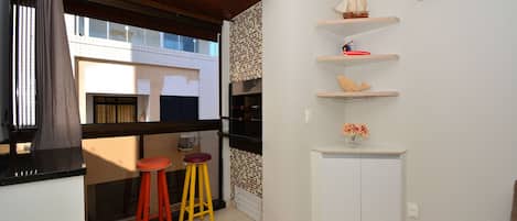 A compact kitchen with a window, two stools, and a white cabinet.