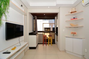 A modern kitchen with a TV, stools, and a cabinet with decorative items.