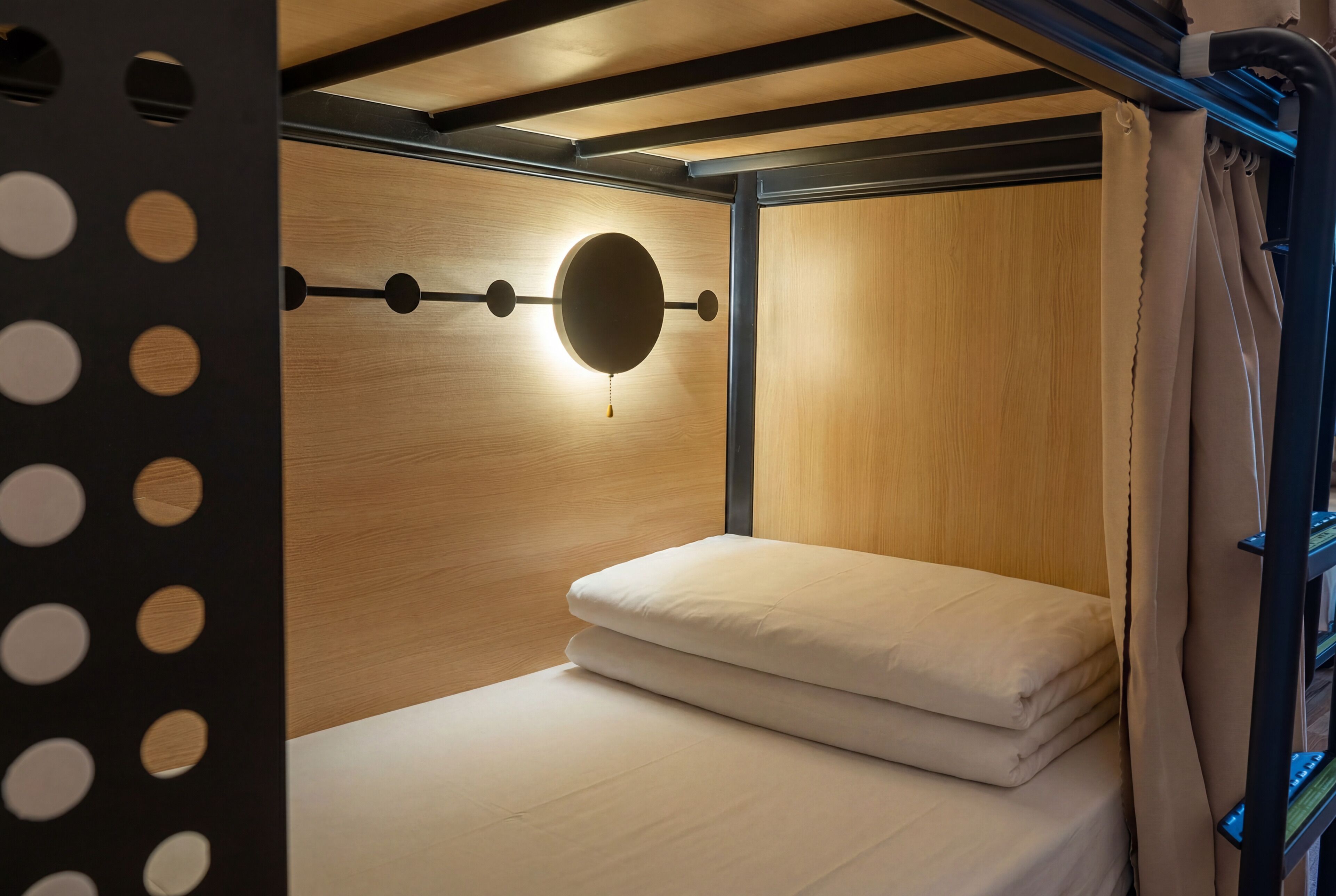 A bunk bed with a circular light fixture on the wall, wooden paneling, and a curtain.
