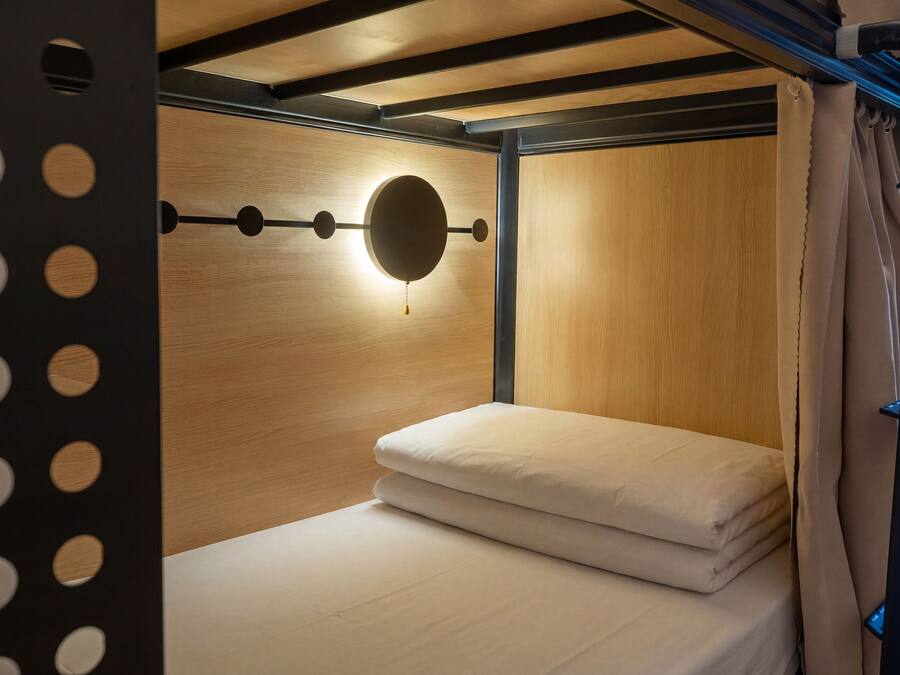 A bunk bed with a circular light fixture on the wall, wooden paneling, and a curtain.