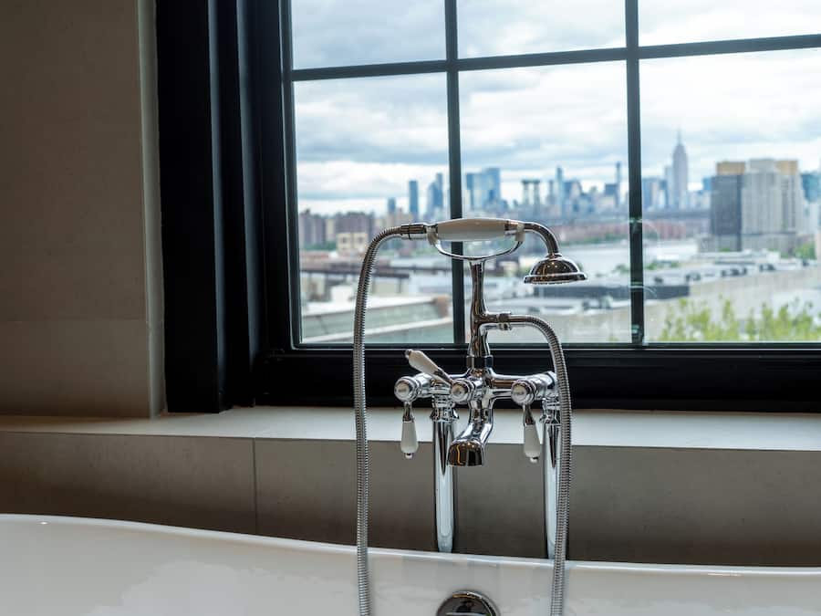 Un baño con bañera, ventana con vistas a un horizonte urbano, y grifo con múltiples mandos.