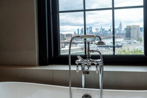 Une salle de bain avec une baignoire, une fenêtre donnant sur le panorama de la ville et un robinet à plusieurs commandes.