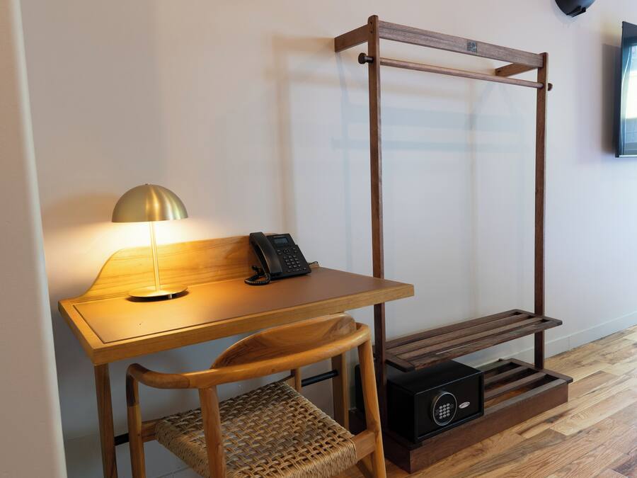 Uma mesa de madeira com uma lâmpada, um telefone, uma cadeira e uma prateleira fixada na parede.