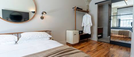 A bedroom with a bed, a round mirror, a wardrobe, and a view of a room with a bed.
