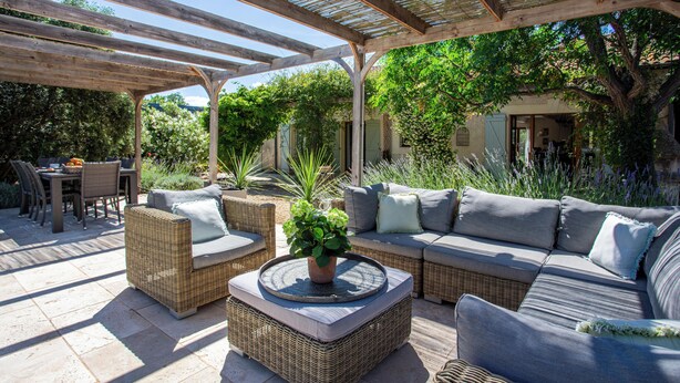 Un espace extérieur aménagé en terrasse, avec des meubles en osier, une table basse ronde agrémentée d’une plante et un coin salon abrité.
