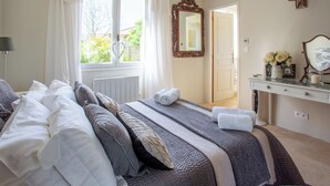 Une chambre à coucher avec un grand lit, une commode, un miroir et une fenêtre avec des rideaux.
