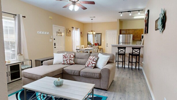 A cozy living room with a sectional sofa, a dining area, and a kitchen in the background.