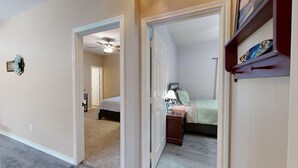 A hallway leading to a bedroom with a bed, a nightstand, and a shelf with decorative items.
