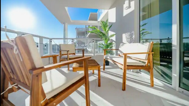 Un balcón con mobiliario de madera, una planta en maceta y vistas de la ciudad.