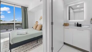 Un dormitorio moderno con cama, un ventanal grande y un baño con espejo y lavabo.