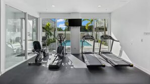 Un gimnasio moderno con cintas de correr, elíptica y bicicleta estática, ventanas amplias y una televisión.