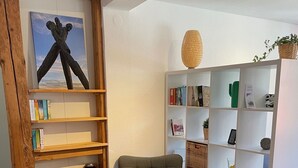 Una habitación con una estantería de madera, un sillón gris y un pequeño reposapiés.
