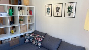 Una sala moderna con un sofá seccional gris, un estante blanco con objetos decorativos y tres cuadros enmarcados.