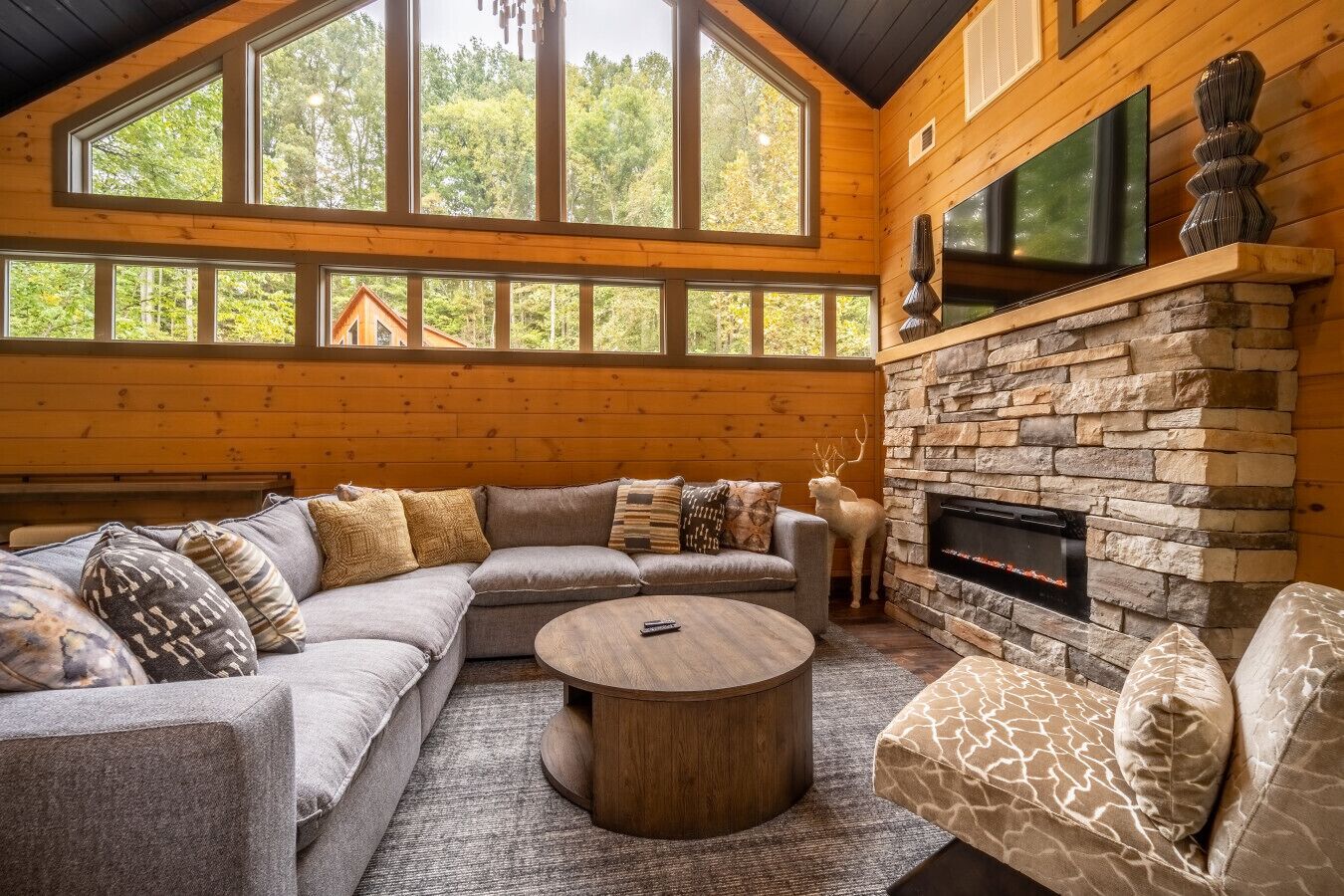 Ein gemütliches Wohnzimmer mit Kamin aus Stein, großen Fenstern und einem Ecksofa.