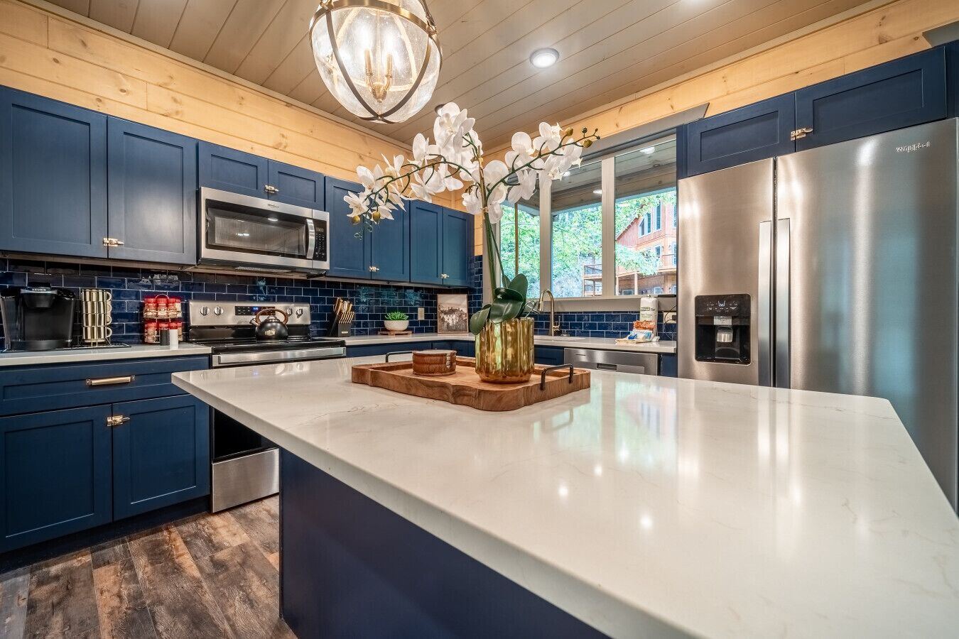 A modern kitchen with blue cabinets, stainless steel appliances, and a large island with a vase of white orchids.