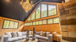 A cozy cabin interior with a wooden ceiling, large windows, a gray sectional sofa, and a decorative deer statue. - Multi-Level Getaway | Pool, Hot Tub and Fireplace (Sevierville)