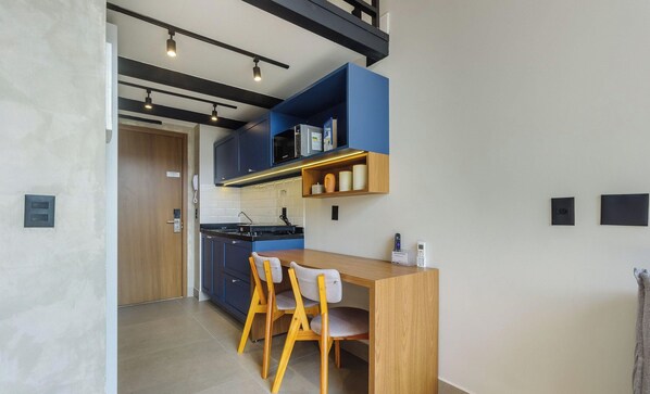 A modern kitchen with a wooden dining table and chairs, a microwave, and a telephone. - Studios in a Building With Pool and Gym in Perdizes - ABY (São Paulo)