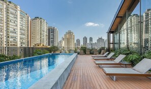 Une piscine sur le toit, dotée de chaises longues et offrant une vue sur la ville.
