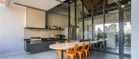 Una cocina moderna con una parrilla empotrada, un refrigerador y un comedor con sillas color naranja.