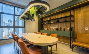Et moderne mødelokale med et langt bord, orange stole, en grøn væg med reoler og en hængende plante.