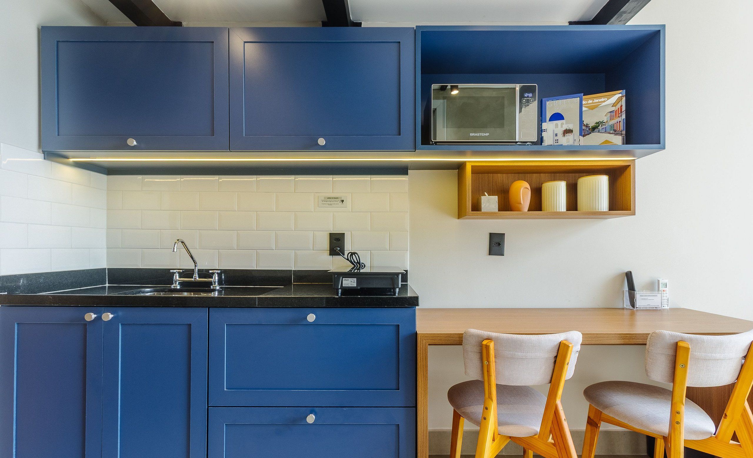 Une cuisine moderne avec des armoires bleues, un comptoir noir et un four à micro-ondes. On y trouve deux chaises en bois et une petite étagère en bois avec des bocaux.