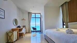 Habitación de hotel con cama, escritorio, silla, perchero y vista al mar.