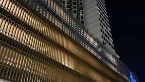 Un edificio moderno con una fachada distintiva de listones verticales y un letrero iluminado destacado.