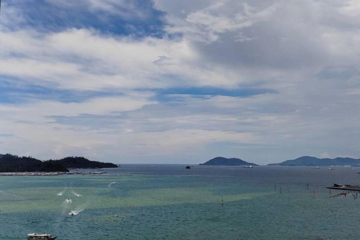 Blick auf die Küste mit ruhigem Wasser, weiter Landzunge und blauem Himmel.