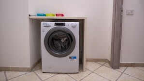 Una lavadora de carga frontal en un cuarto de lavado con piso de baldosas y un estante encima.