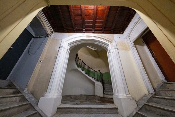 A grand staircase with a wooden ceiling, white columns, and a green railing.
