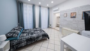 Un dormitorio con cama, escritorio y silla. Hay una ventana con cortinas, un radiador y un aire acondicionado instalado en la pared.