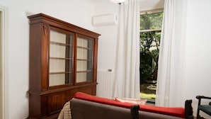 A room with a wooden cabinet, a sofa, and a view of greenery outside. - Casa delle camelie - Two Bedroom Apartment, Sleeps 6 (Naples)