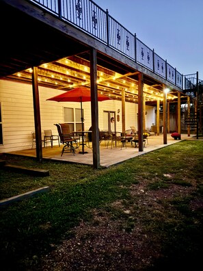 Un espace extérieur aménagé en terrasse, avec des poutres en bois, des tables, des chaises et des guirlandes lumineuses.