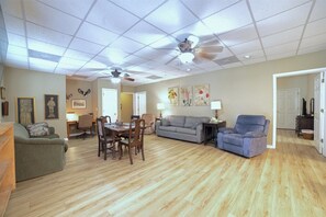 Uma sala de estar ampla com área de jantar, um sofá cinza, uma poltrona azul e um ventilador de teto.