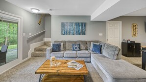 Una sala moderna con un sofá seccional gris, una mesa de centro de madera y una escalera que conduce a un balcón.