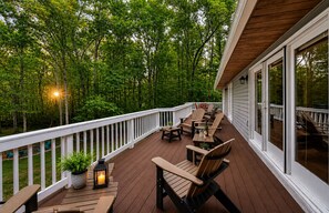 A wooden deck with outdoor furniture, a railing, and a view of a forested area.