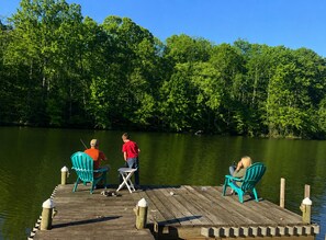 A wooden dock with three chairs, a small table, and a person fishing.