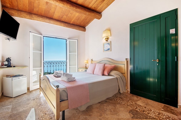 A bedroom with a bed, a green door, a TV, a small white appliance, and a balcony.
