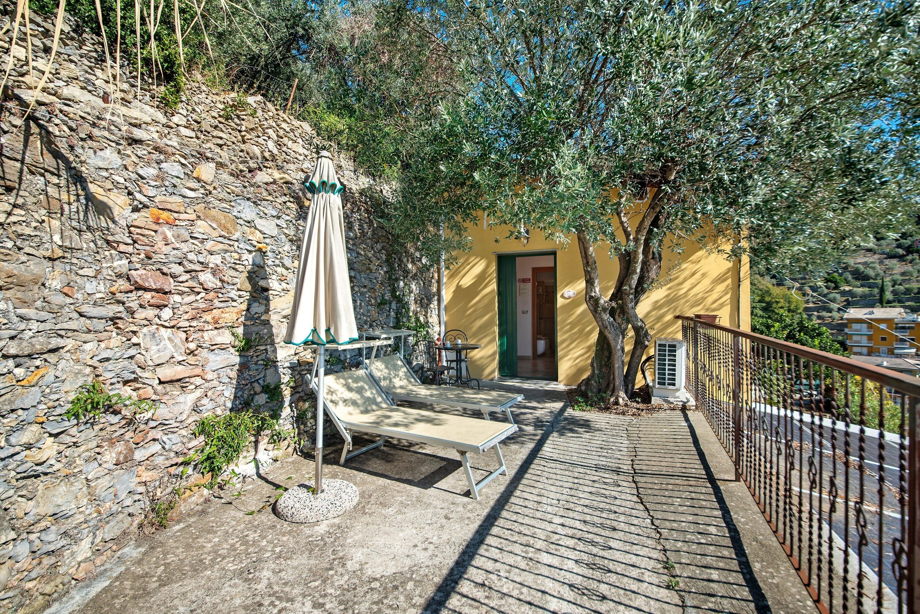Un muro de piedra, un edificio amarillo con una puerta y un árbol.